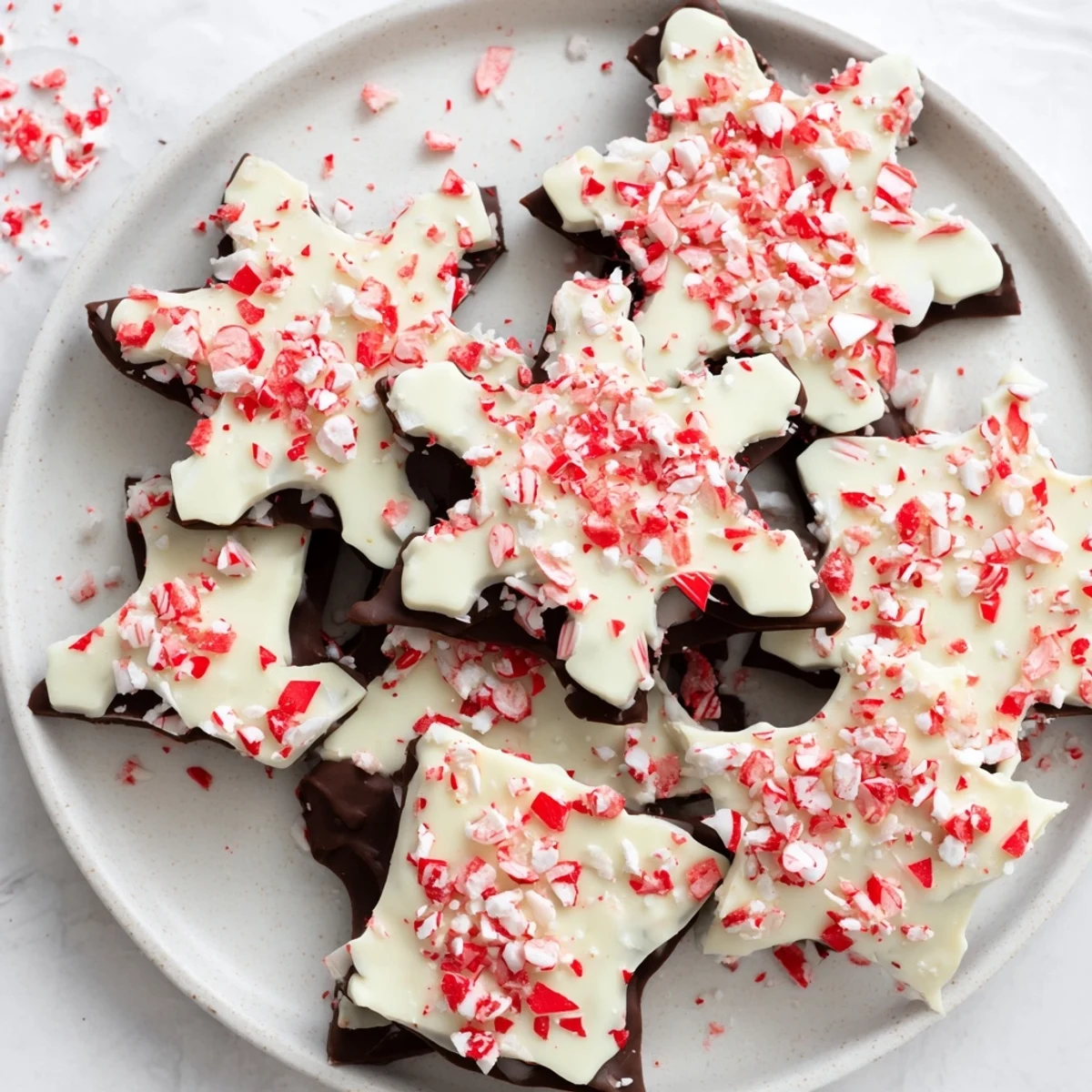 Bright pink peppermint bark snowflakes on a platter, showcasing layers of dark and white chocolate.