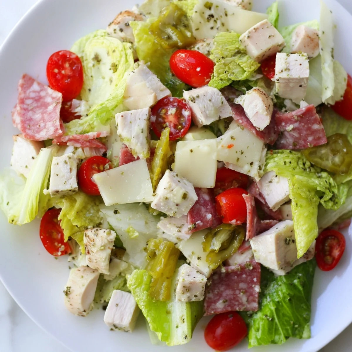 A close-up of the Italian Deli Chopped Chicken Salad on a white plate, featuring vibrant chopped romaine, diced chicken, salami, and provolone cheese.  