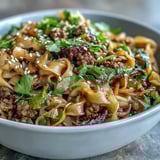 Bright green onions and fresh cilantro garnish the bowl of Asian fusion noodles, completed with sesame seeds.