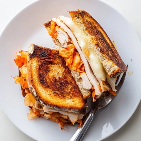Golden melted cheddar spills over a Kimchi Turkey & Cheddar Toasted Grilled Cheese, ready to eat.
