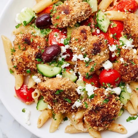 Golden crispy chicken bites rest atop penne pasta tossed with fresh tomatoes, cucumbers, olives, and creamy feta cheese in this Greek-inspired dish.