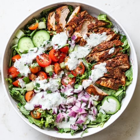 A vibrant Chicken Shawarma Salad Bowl with spiced, juicy chicken atop crisp greens, cucumbers, tomatoes, and a drizzle of tangy garlic sauce.