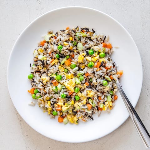 Black garlic fried rice is tossed with scallions and sesame oil, steaming fragrantly in a skillet beside a small bowl of toppings.