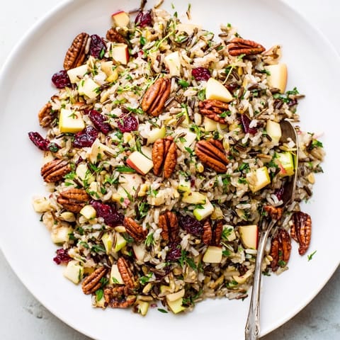 Wild Rice Harvest Salad in a rustic bowl, showcasing glossy cranberries and golden toasted pecans on nutty grains.