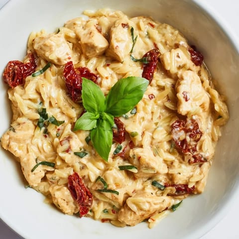 A rustic skillet of Tuscan Chicken Orzo featuring tender chicken, sun-dried tomatoes, and wilted spinach for a savory meal.