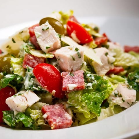 Serving suggestion for the hearty Italian Deli Chopped Chicken Salad, with a colorful mix of cherry tomatoes, pepperoncini, and a tangy herb dressing.  