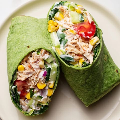 Sliced in half, the BBQ Chicken Salad Wrap reveals colorful layers of sweet corn, tangy sauce, and fresh veggies.